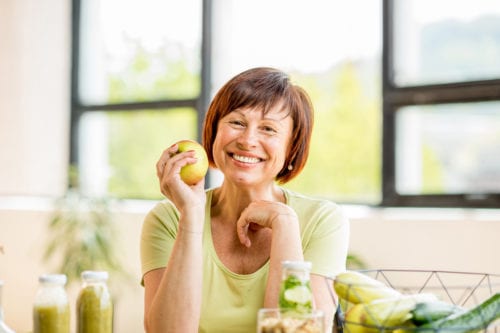 A smiling middle-aged woman with an apple at home. She is happy she found a diabetes doctor in Idaho Falls and Pocatello at Rocky Mountain Diabetes Center.