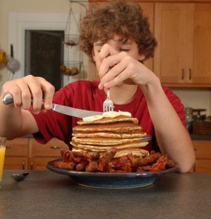 Young boy eating large stack of pancakes and bacon, breakfast symptoms of Prader-Willi Syndrome which is treated by Dr. Joshua Smith, the region's only pediatric endocrinologist based in Idaho Falls with an office in Pocatello.