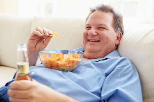 Overweight man smiling as he is eating potato chips, which can lead to hypertention that can be treated by our endocrinologists in Idaho Falls and Pocatello.