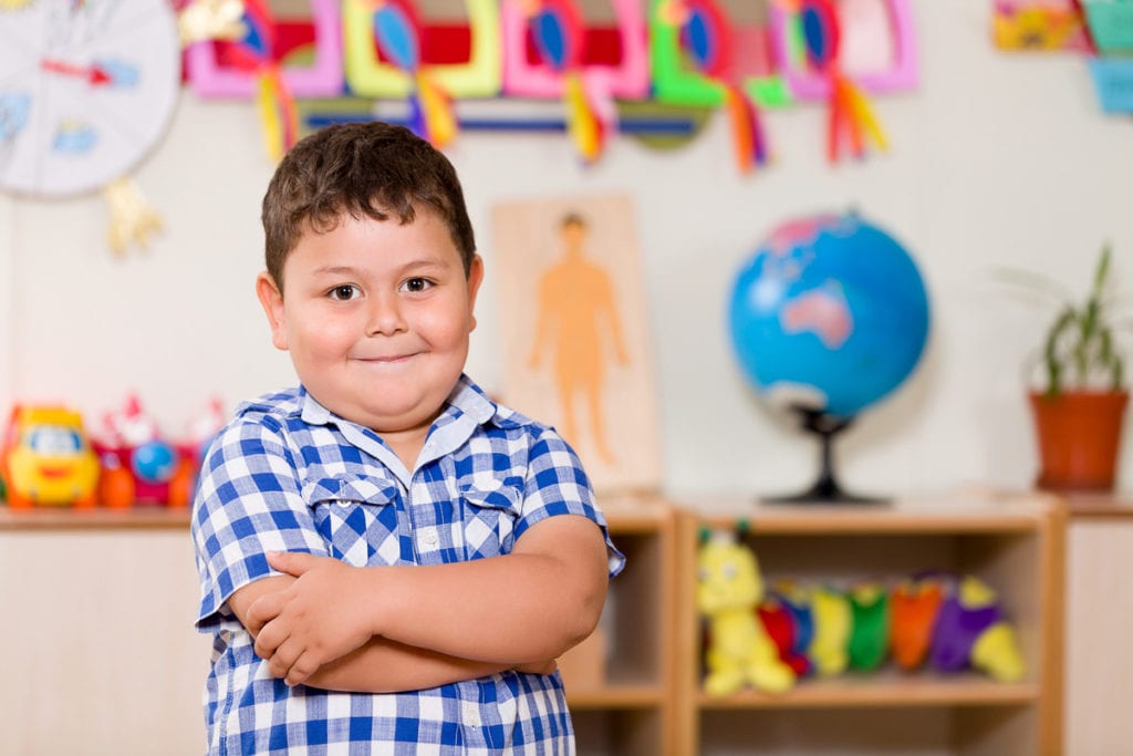 Young overweight child with type 2 diabetes folding his arms and smiling at his day care facility.