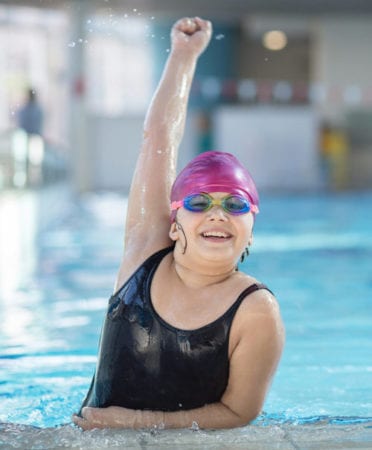 Young female swimmer smiling and holding fist up high, with weight gain issues receiving treatment from Dr. Josua Smith, the region's only pediatric endocrinologist in Idaho Falls and Pocatello.