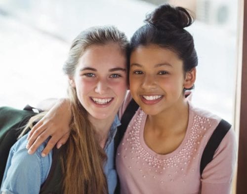 Two young teenage girls at school discussing early or delayed puberty treatment treatment by Dr. Joshua Smith, a pediatric endocrinologist in Pocatello and Idaho Falls.