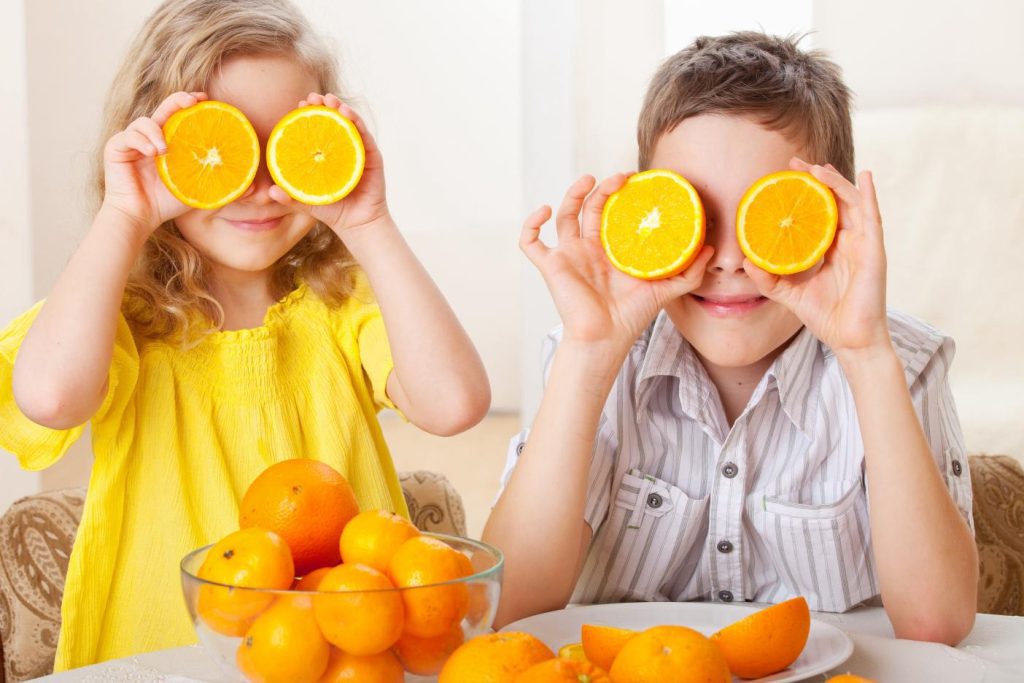 Two kids with orange slices held up tot heir eyes like glasses.